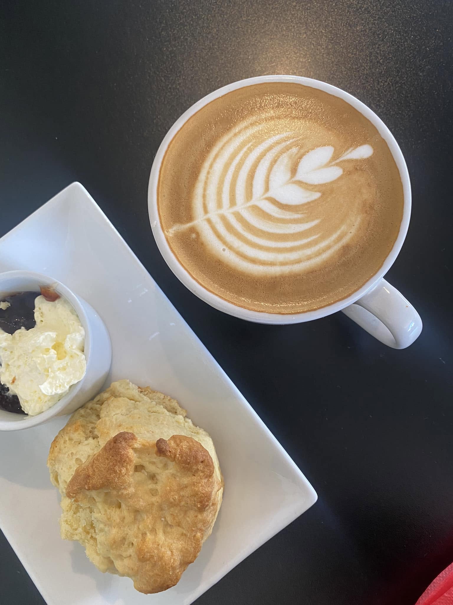 Warm scone with jam and cream served beside a flat white